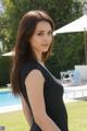 A woman in a black dress posing by a pool.