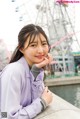 A woman leaning against a wall with a ferris wheel in the background.