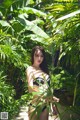 A woman in a black bikini standing in a tropical garden.