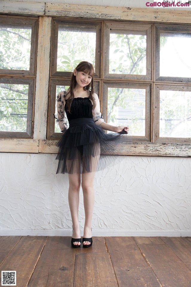A woman standing in front of a window wearing a black dress.