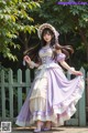 A woman in a purple and white dress and hat posing for a picture.